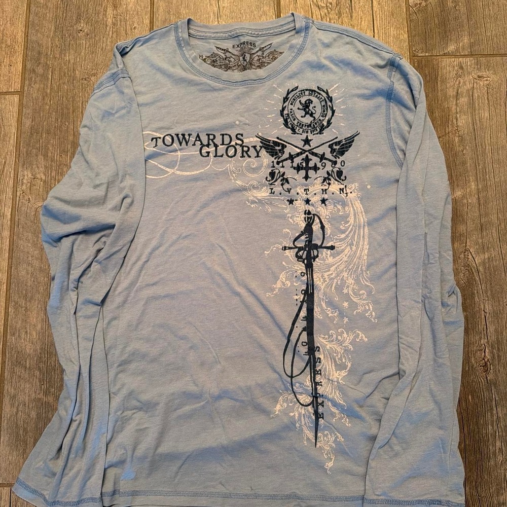 This is a light blue long-sleeve graphic t-shirt featuring a prominent sword